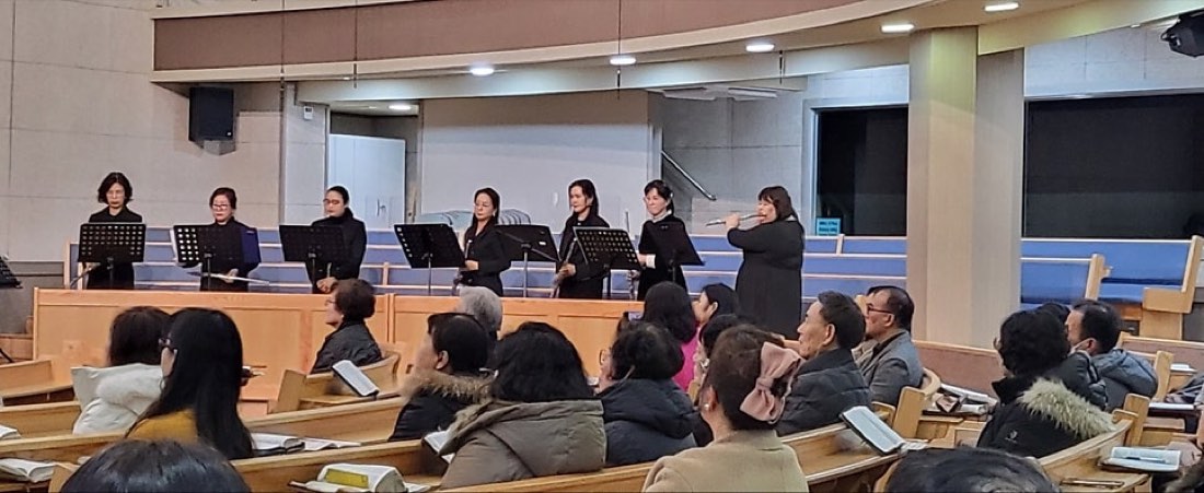 교회 강단 앞에서 플루트 연주자들이 일렬로 서서 연주하는 모습